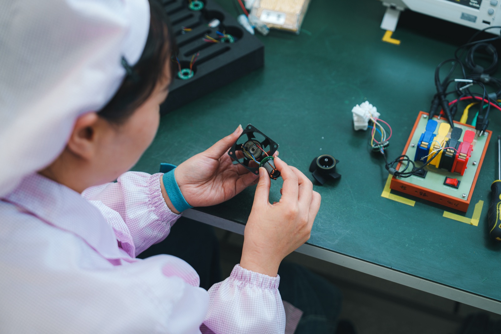 Technician testing DC cooling fan electrical characteristics including startup current and control signals at an ESD-protected test bench