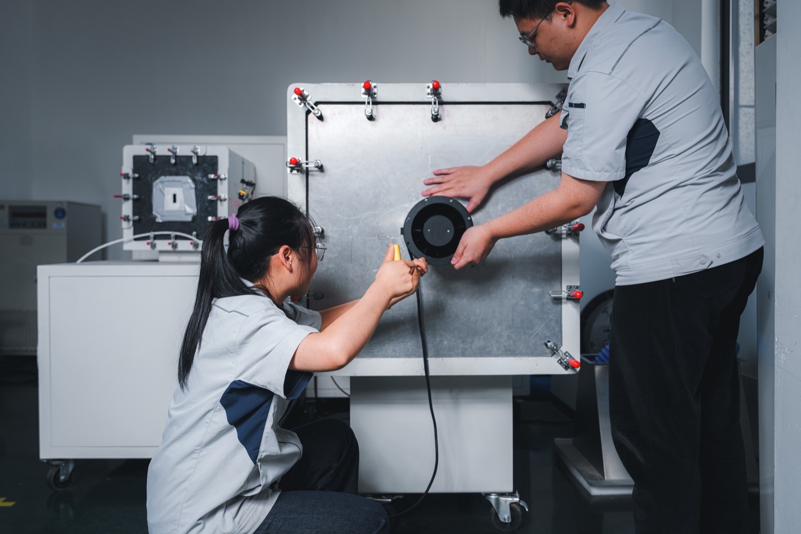Technicians conducting standardized fan performance testing using a sealed plenum chamber with measurement probes